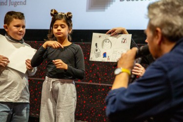 Ein Mädchen gebärdet im Kinosaal beim KinderKinoFest Düsseldorf.
