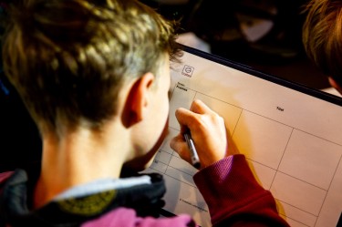 Der Hinterkopf eines Jungen, er beschriftet ein Storyboard aus Papier.
